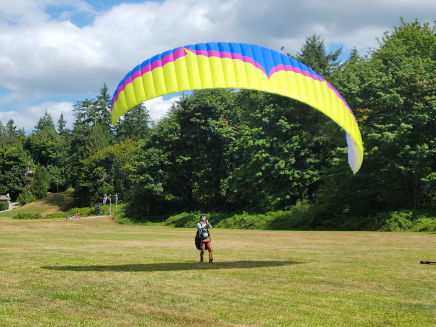 Jonathan with a colorful paraglider in a grassy field with trees in the background