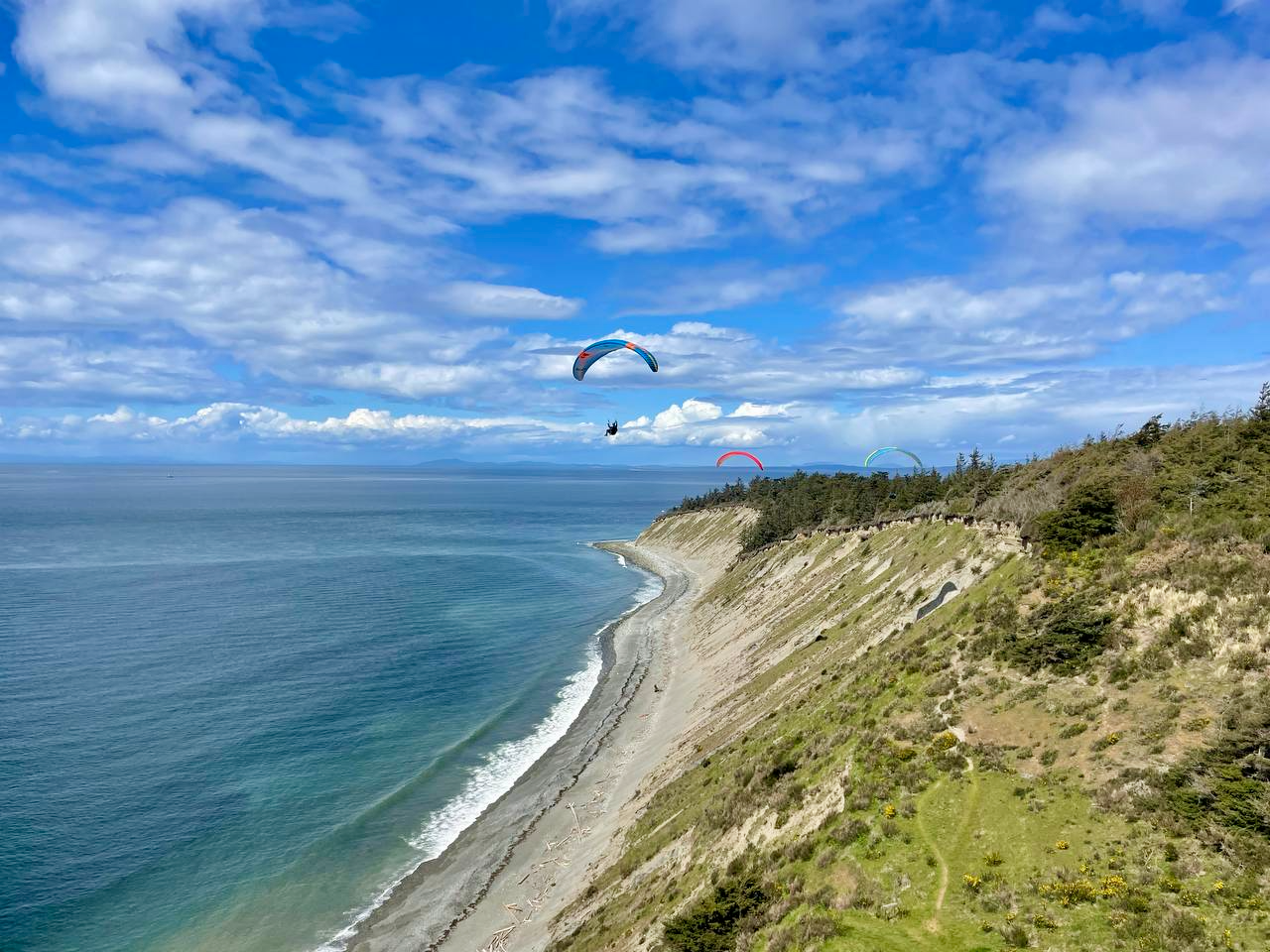 Paragliders flying over a coastal landscape with blue sky and ocean.